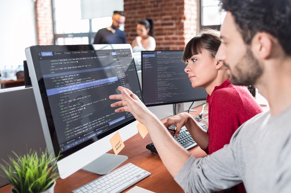 An instructor teaching web design coding on a desktop to a female student in an institute.